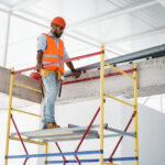 Young handsome builder climbing on scaffolding at construction site Laudo Técnico Andaimes