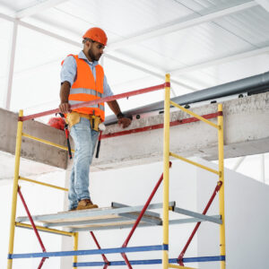 Young handsome builder climbing on scaffolding at construction site, close up